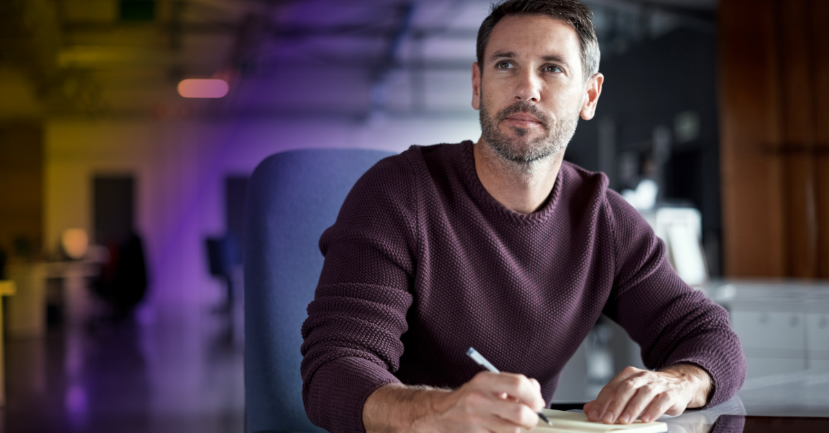 Man seated at a desk and writing on a notepad